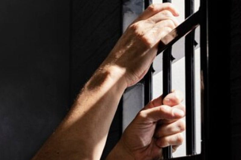 Unas manos en una reja de la cárcel - Responsabilidad de la persona jurídica y gestión de riesgos penales
